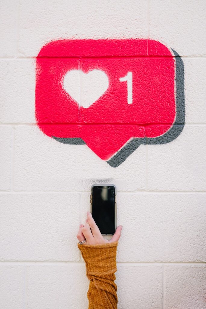 Arte imitando um stencil de uma mão segurando um celular e o balão de likes de Instagram apontando uma curtida