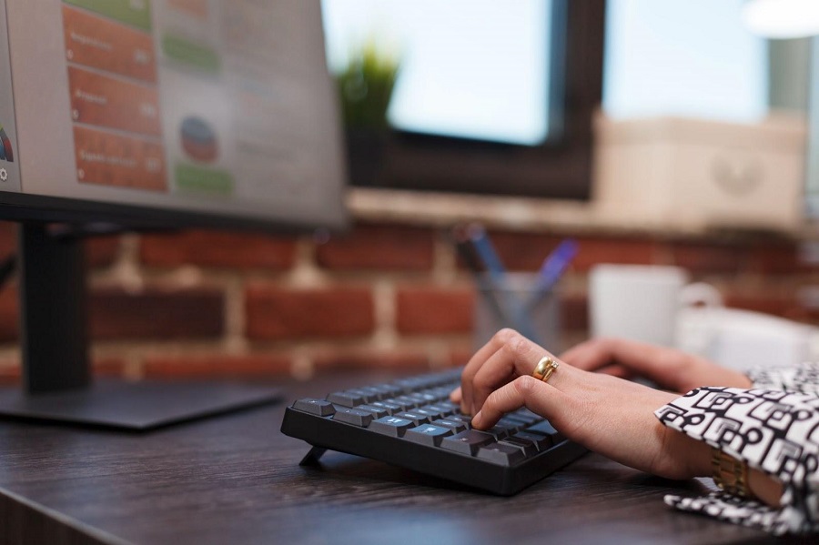 Mãos femininas digitando em um teclado acoplado a um monitor