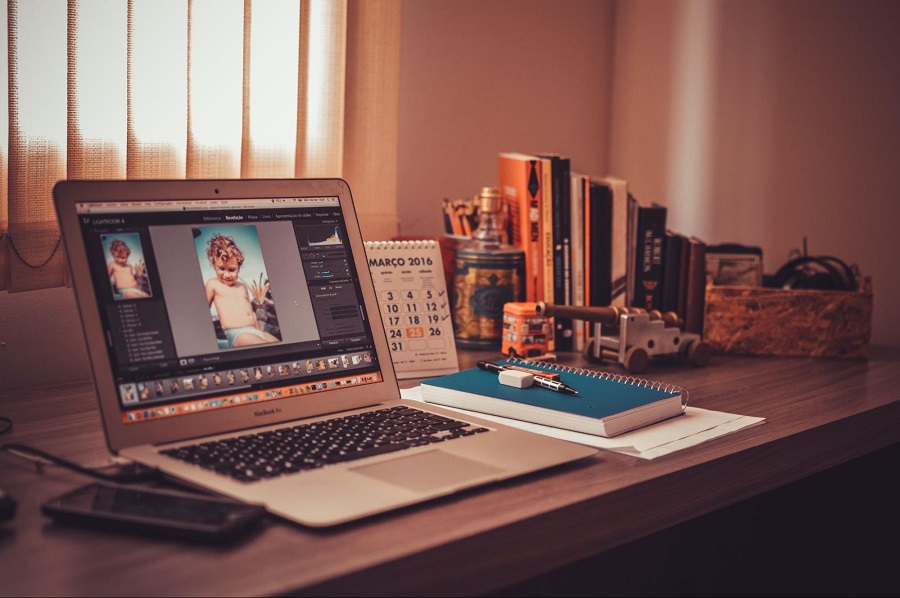 Foto de uma mesa de trabalho com um notebook ligado e algum programa editor de imagem aberto na área de trabalho