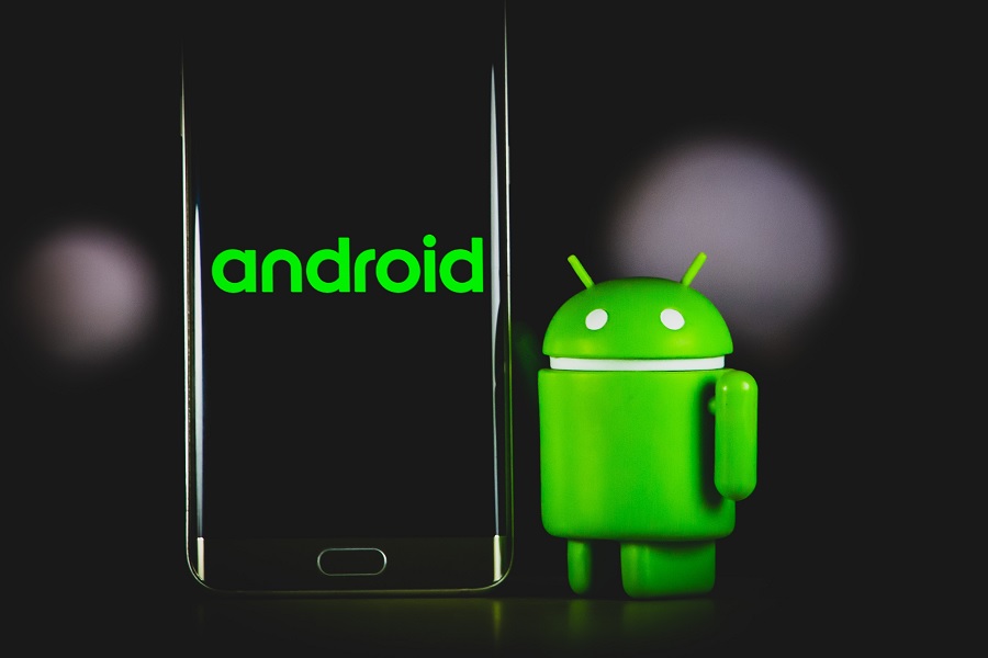 Mascote da Android ao lado de um smartphone preto.