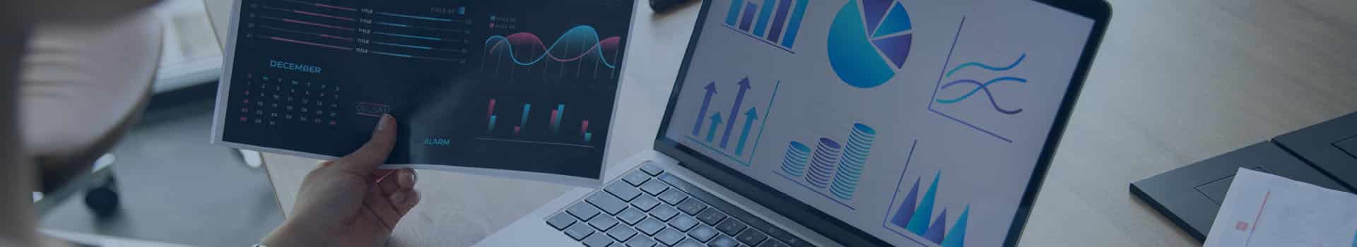 Pessoa analisando dashboards do Power BI em um laptop e impressos, comparando a visualizações de dados e gráficos.