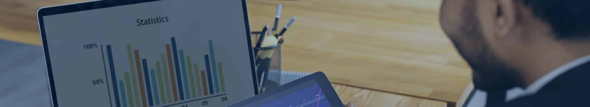 Profissional no escritório analisando gráficos em um tablet e laptop usando a ferramenta Power BI gratuita para visualização de dados.
