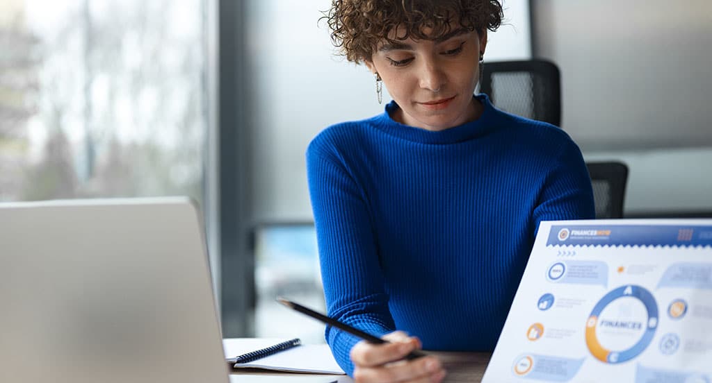 Aluna de blusa azul e cabelo curto analisando gráficos financeiros, destacando a importância de estudar business intelligence na faculdade para aprender sobre tomada de decisões.