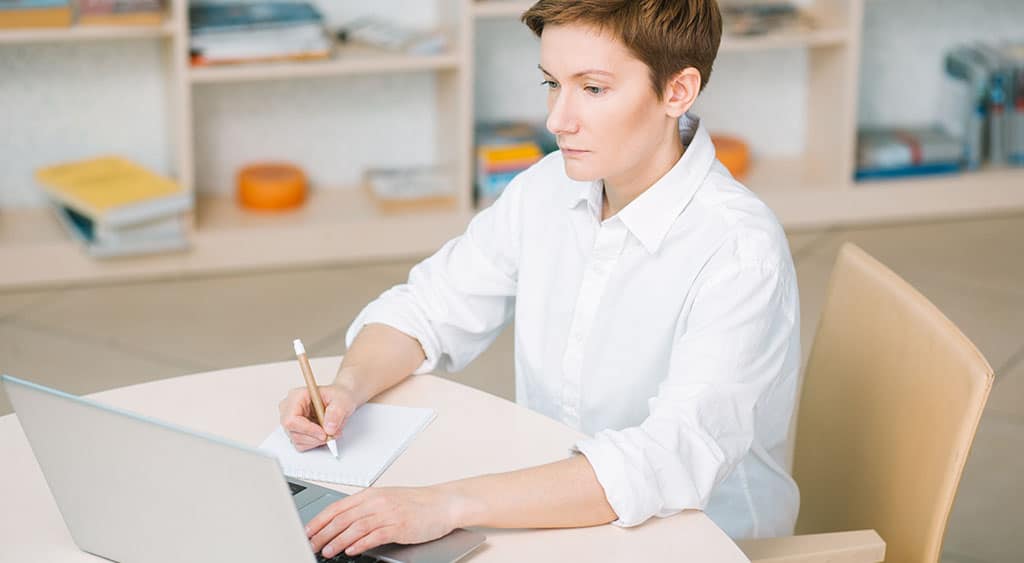 Profissional mulher de blusa branca e cabelo curto em um laptop, representando a busca pelos melhores cursos de BI para aprimorar habilidades analíticas e estratégicas.