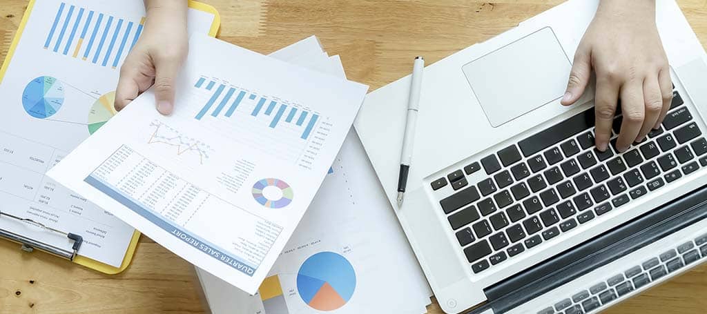 Profissional analisando relatórios financeiros com gráficos em papel e laptop, representando a escolha entre Google Data Studio vs Power BI para análise de dados.