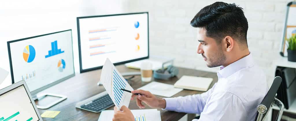 Profissional analisando relatórios e gráficos em múltiplas telas, representando a área de BI e a utilização de dados para tomadas de decisão estratégicas.