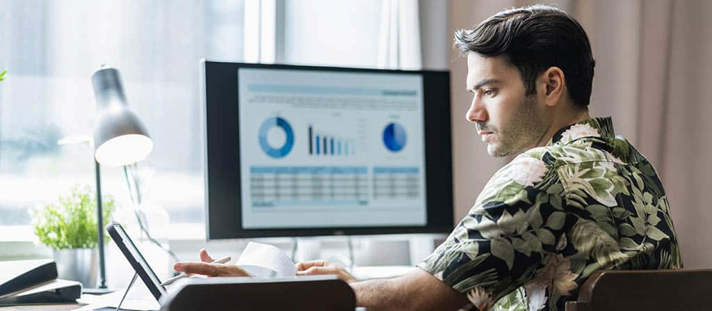Profissional analisando gráficos em tela e tablet, ilustrando como trabalhar com Business Intelligence na tomada de decisões estratégicas.