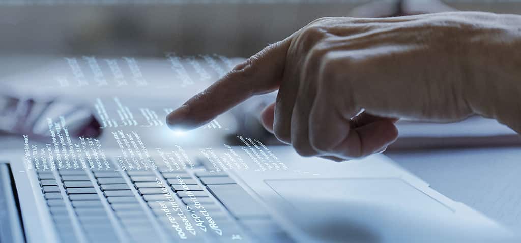 Mão interagindo com interface digital sobre teclado de laptop, ilustrando o que é virtualização e o conceito de ambientes computacionais virtuais.