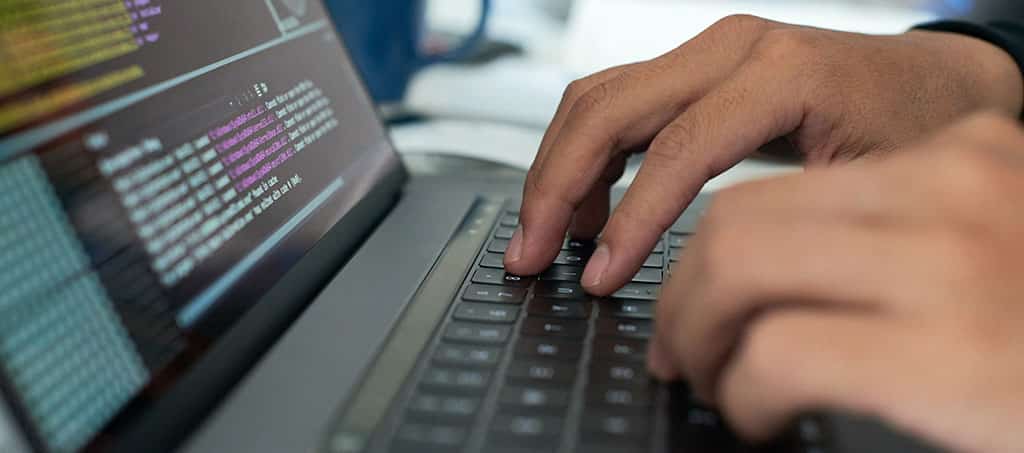 Desenvolvedor digitando código em um laptop, focado em programação back-end.