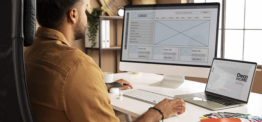 Desenvolvedor de aplicativos trabalhando com computador no design e estrutura de um app em um monitor grande, com protótipos e layout em exibição.