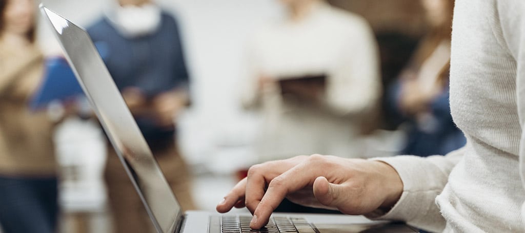 Estudante digitando em um laptop em ambiente acadêmico, representando uma faculdade de redes de computadores e aprendizado colaborativo.