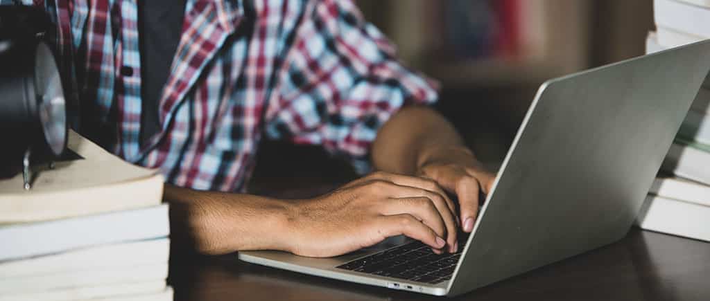 Estudante concentrado em sua pós-graduação em redes, utilizando laptop em meio a livros em uma biblioteca.