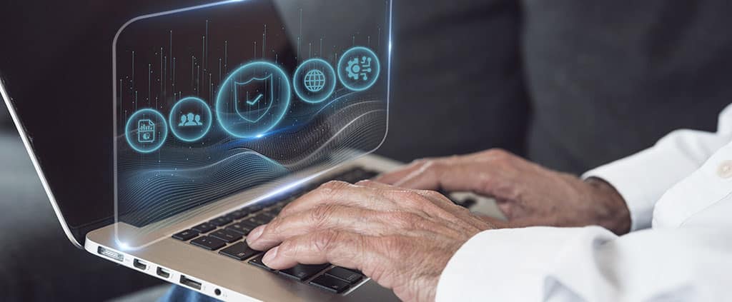 Mãos usando um laptop com interface digital, ilustrando uma das desvantagens da virtualização, que é a necessidade de manutenção e de profissionais qualificados.