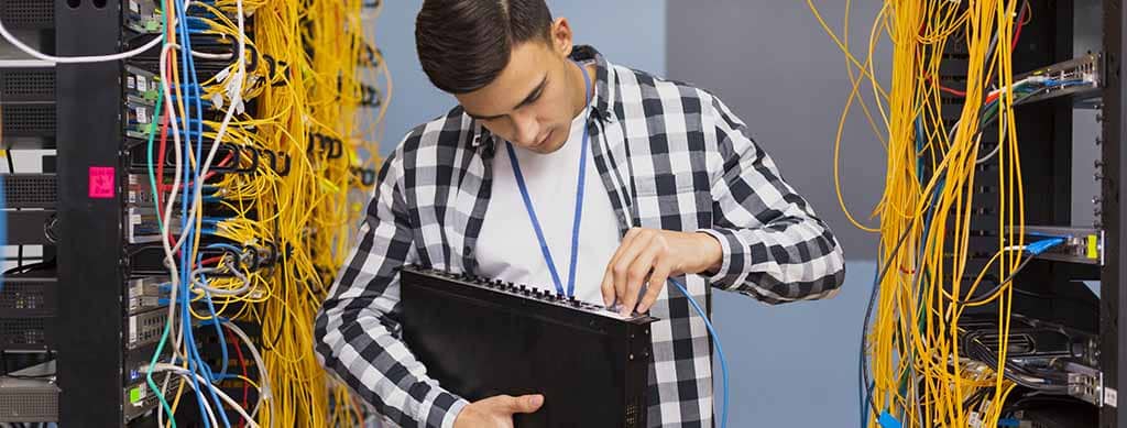 Engenheiro de redes conectando cabos em um data center, ilustrando a habilidade de manutenção e configuração de infraestruturas de rede.