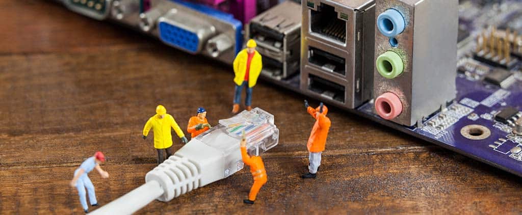 Miniaturas de trabalhadores conectando um cabo de rede a uma placa-mãe, simbolizando o que é a engenharia de redes e sua importância na conectividade digital.