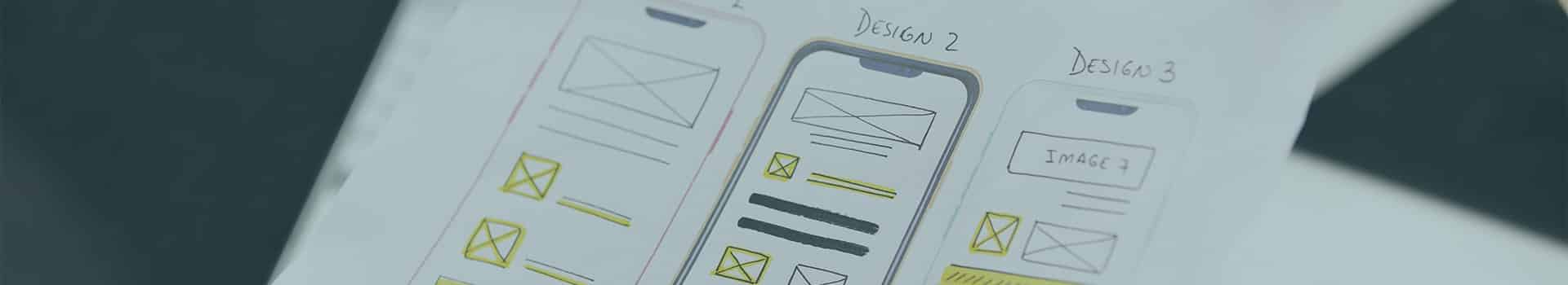 Mãos segurando um esboço impresso de interface para app, representando o processo de desenvolvimento mobile e design de experiência do usuário.