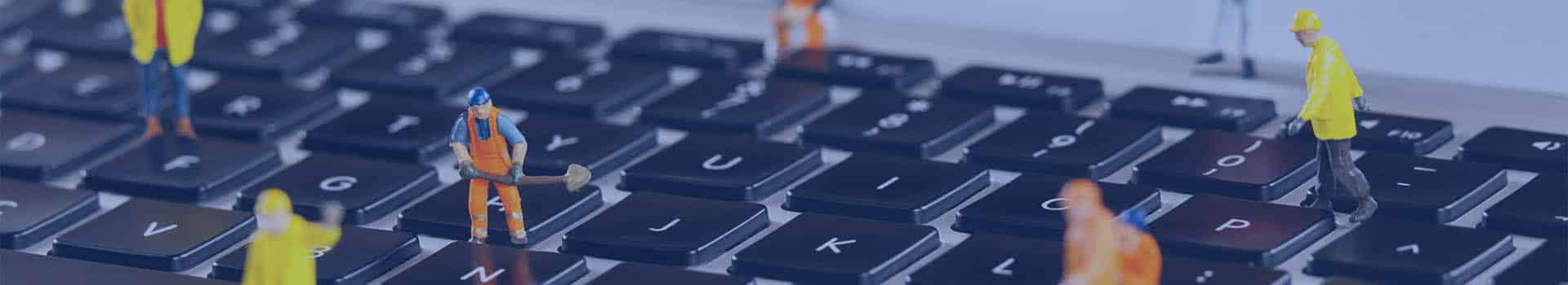 Trabalhadores em miniatura simulam a manutenção de um teclado de laptop, representando a engenharia de redes e sua importância na conectividade digital.