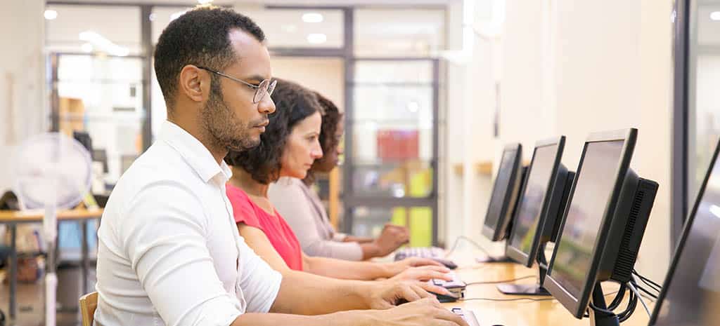 Alunos focados em computadores durante um curso de desenvolvedor mobile, aprendendo programação e desenvolvimento de aplicativos.