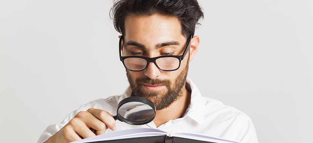 Homem analisando um livro com uma lupa, representando a pesquisa sobre como fazer jogos para Android e o aprofundamento no desenvolvimento mobile.