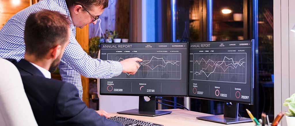 Profissionais analisando dados em monitores duplos com gráficos de desempenho no Checkmk.