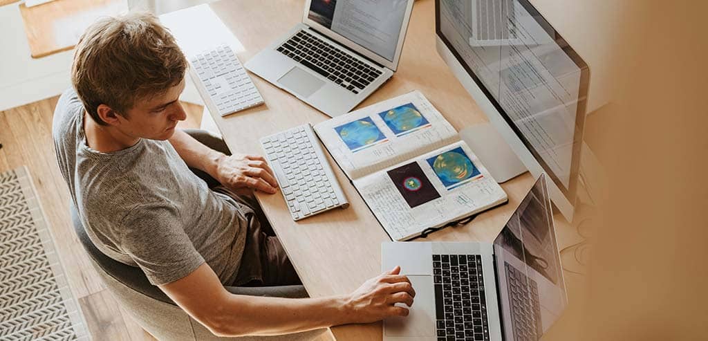 Profissional homem estudando em um ambiente organizado com múltiplos dispositivos, representando um aluno de um bom curso de arquitetura de software.