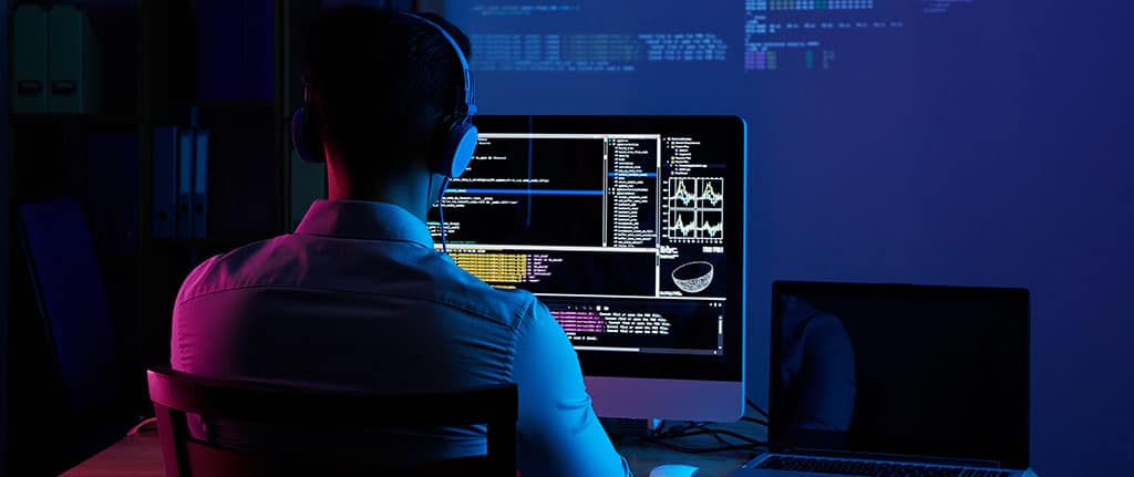 Programador estudando em um curso back-end gratuito, com códigos exibidos na tela do computador e projetados na parede.