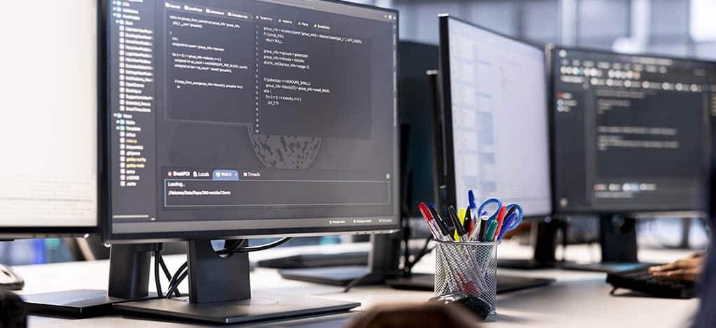 Profissional de TI monitorando servidores e otimizando código em múltiplas telas, representando o gerenciamento de rede com OpManager.