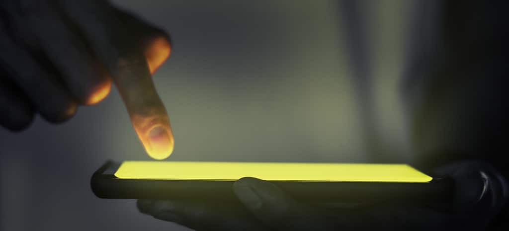 Mão interagindo com a tela iluminada de um smartphone, simbolizando o trabalho de um desenvolvedor no desenvolvimento de aplicativos.