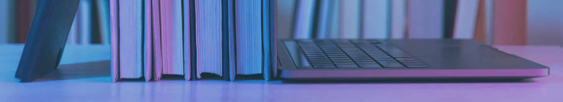 Livros de arquitetura de software ao lado de um laptop com uma estante de livros ao fundo, simbolizando a importância dos estudos e do conhecimento teórico.