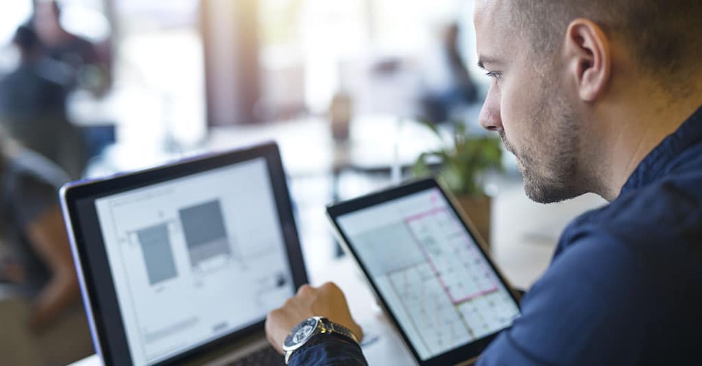 Profissional analisando um exemplo de projeto de arquitetura de software em um laptop e tablet, planejando soluções técnicas para desenvolvimento.