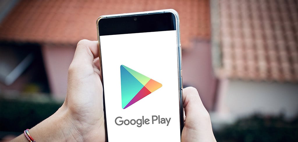 Mãos segurando um smartphone exibindo o logo da Google Play, ilustrando parte do processo de como criar um aplicativo no Play Store grátis.