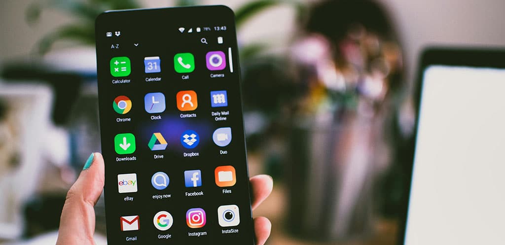 Mão segurando um smartphone com diversos aplicativos, representando o processo de publicar e lançar um app na Play Store.