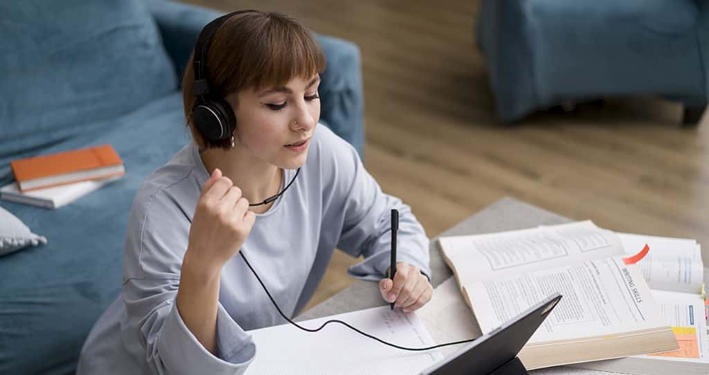 Estudante pesquisando sobre a formação do arquiteto de software, anotando ideias enquanto usa um tablet e fones de ouvido.