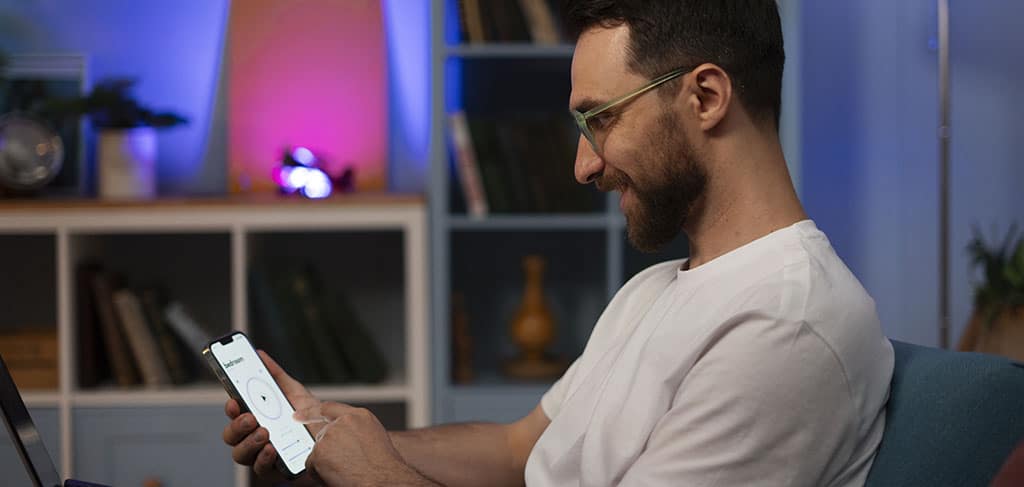 Homem no sofá da sala de casa sorrindo enquanto usa um smartphone, representando as vantagens de registrar um aplicativo de forma oficial e segura.