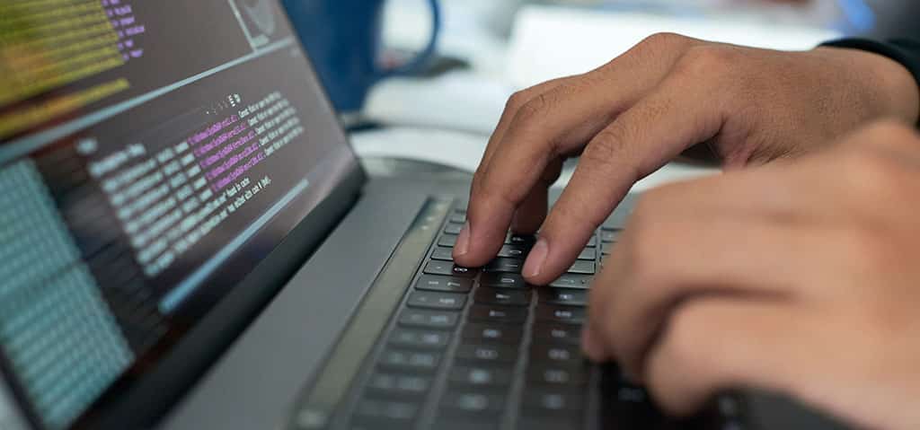 Mãos digitando código em um laptop, ilustrando o que um arquiteto de software faz ao projetar e desenvolver sistemas eficientes e escaláveis.