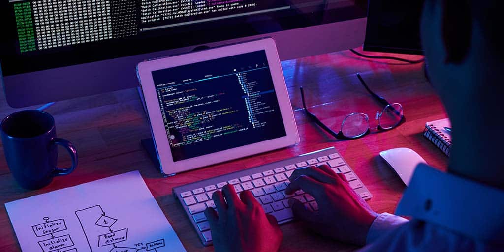 Desenvolvedor programando com diagrama de fluxo ao lado, destacando a importância da arquitetura de software no planejamento e estruturação de sistemas.