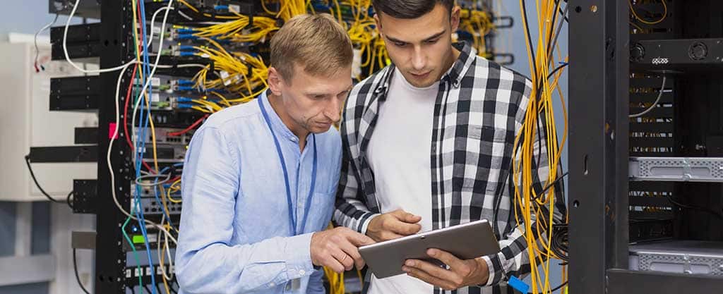 Profissionais de TI analisando redes em um data center, ilustrando o que é Spiceworks e como essa ferramenta auxilia no monitoramento de infraestruturas.