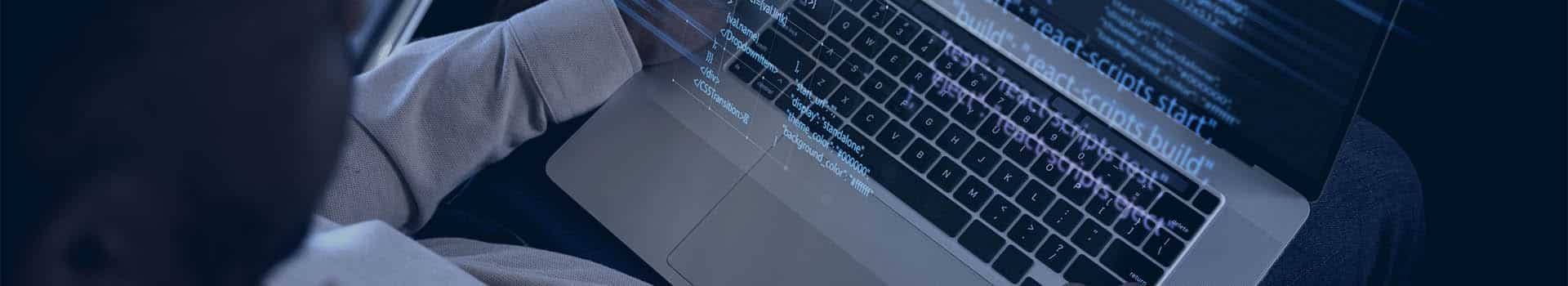 Pessoa programando em um laptop com códigos projetados na tela, representando a cooperação entre arquitetura de hardware e software.