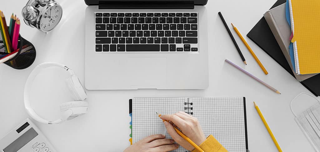 Aluno fazendo anotações, representando alguém estudando para um curso virtualização de servidores, com laptop e materiais de estudo na mesa.